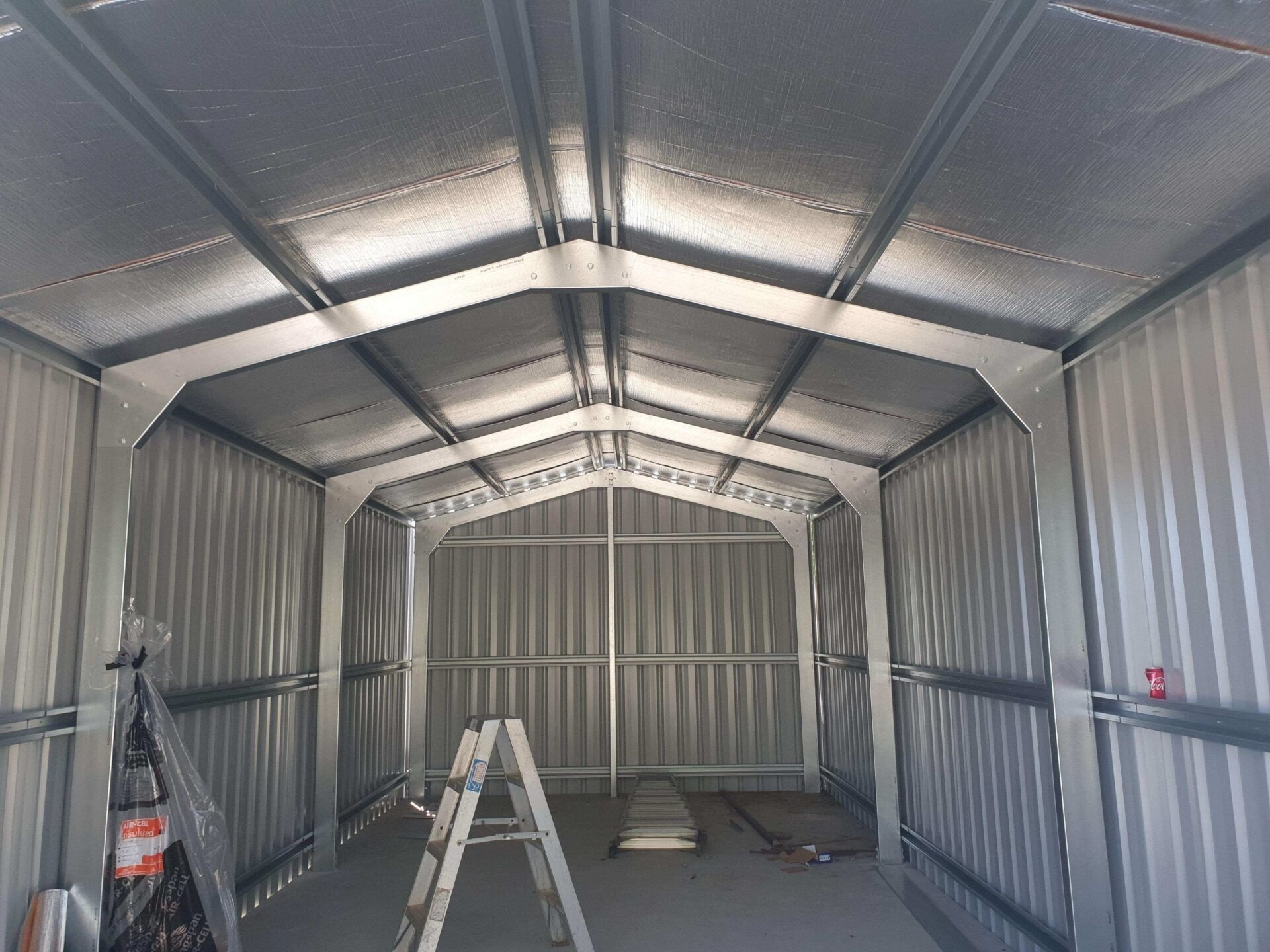 Bare interior of a newly built steel shed showing high roof purlins and wall frames ready for vertical storage solutions